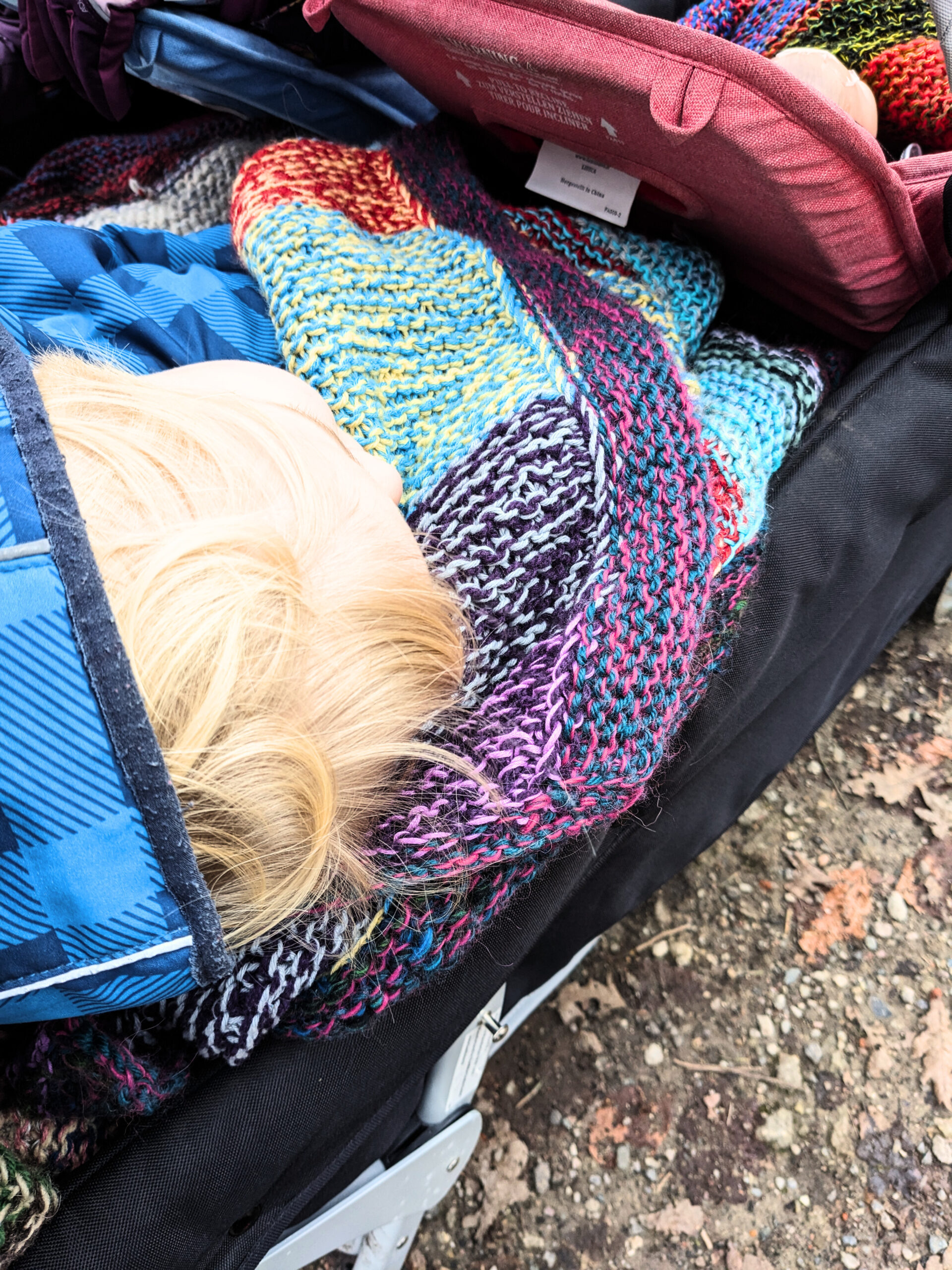 Ein Krippenwagen, in dem ein Kind schläft, eingemummelt in eine bunte Wolldecke