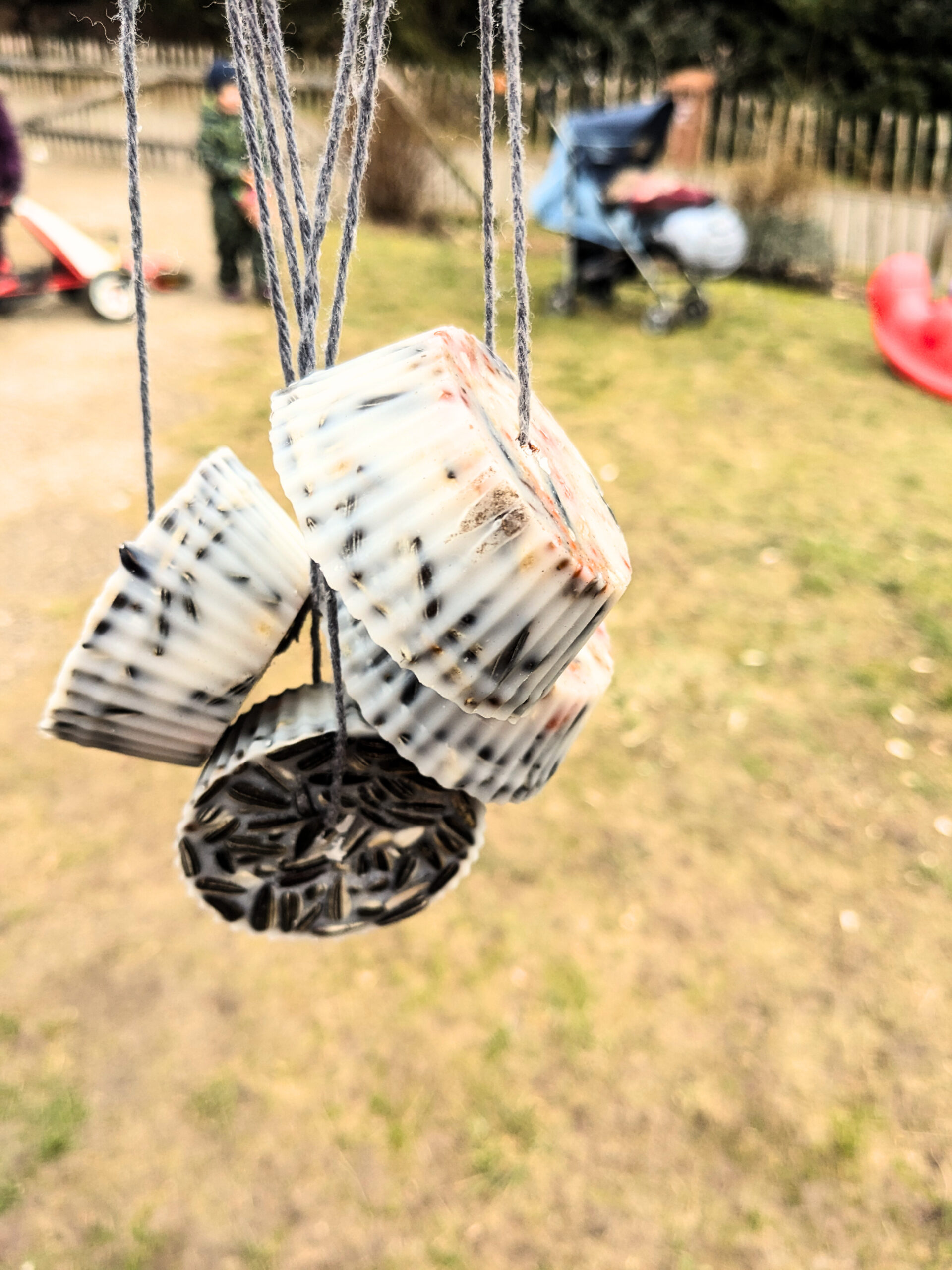 Im Hintergrund spielen Kinder in einem Garten im Vordergrund selbstgemachtes Vogelfutter
